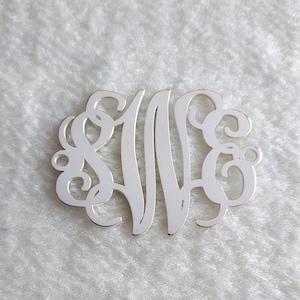 May include: Silver monogram charm with a cursive letter design. The charm is oval shaped and has a hole at the top for attaching to a necklace or bracelet.