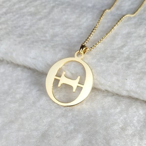 Op de afbeelding: Een gouden ketting met een hanger in de vorm van de letter "O" met een kleinere "H" uitgesneden in het midden.
