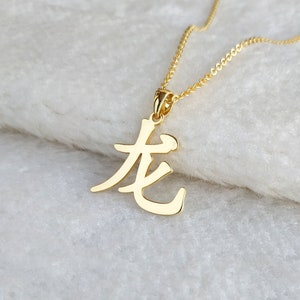 May include: Gold necklace with a pendant featuring the Chinese character for "long" in a stylized font.