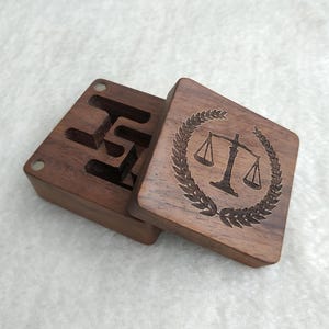 以下が含まれることがあります： ヒンジ付きの蓋が付いた木製の箱。蓋には、月桂樹の輪で囲まれた天秤が刻まれています。箱には、小さな物を収納するための仕切りがあります。