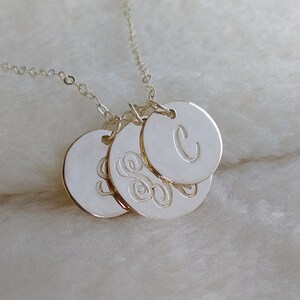 May include: Silver necklace with three round pendants. The largest pendant has the letter "C" engraved on it. The two smaller pendants have a monogram design.