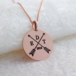 May include: Rose gold necklace with a round pendant featuring two crossed arrows with the letters "E", "D", and "T" and the year "2016" engraved on the pendant.