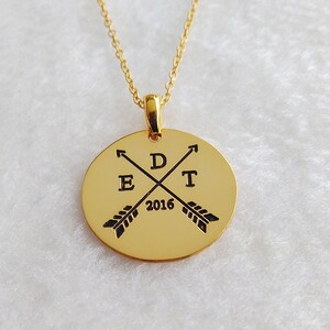 May include: Gold necklace with a round pendant featuring two crossed arrows with the letters "D", "E", "T" and the year "2016" engraved on it.