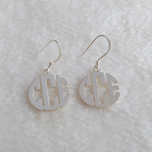 Puede incluir: Un par de pendientes de monograma de plata con las letras "CCC" recortadas del diseño circular.