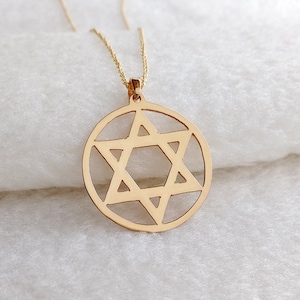 May include: A gold chain necklace with a pendant featuring a Star of David design. The pendant is a circle with a six-pointed star cut out of the center.