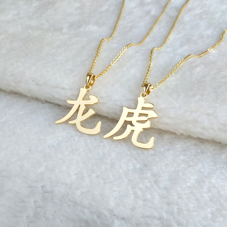 May include: Two gold necklaces with Chinese character pendants. The characters are "龙" and "虎", which translate to "dragon" and "tiger".