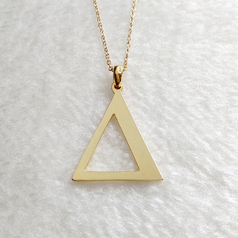 Peut inclure: Un collier avec un pendentif en forme de triangle en or et une cha&icirc;ne d&eacute;licate. Le triangle est creux et a une finition lisse et polie.
