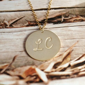 May include: Gold necklace with a round pendant featuring the initials "LC" in cursive script.