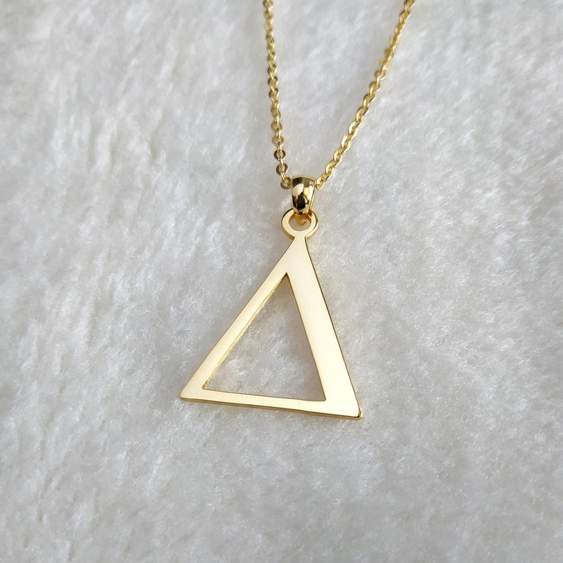 Peut inclure: Un collier en or avec un pendentif en forme de triangle. Le triangle est creux et a une finition lisse et polie.