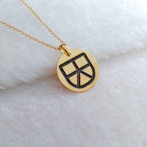 May include: A gold necklace with a round pendant featuring a black shield design.