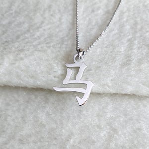 May include: A silver necklace with a pendant shaped like the Chinese character for "horse".
