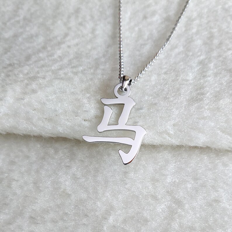 May include: A silver necklace with a pendant shaped like the Chinese character for "horse".