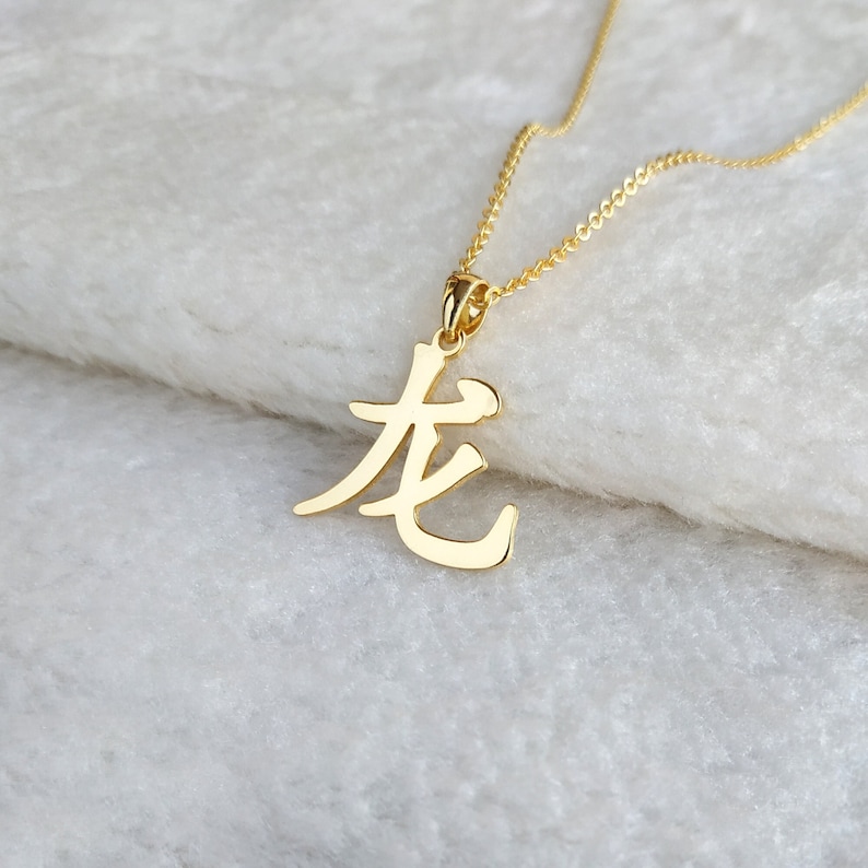 May include: Gold necklace with a pendant featuring the Chinese character for "long" in a stylized font.