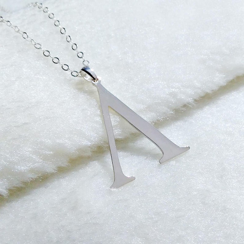 Peut inclure: Un collier en argent avec un pendentif en forme de lettre grecque Delta.
