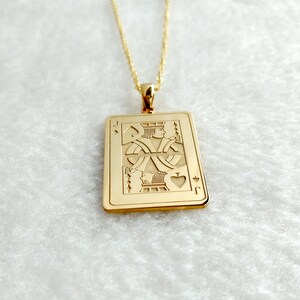 May include: Gold pendant necklace. The rectangular pendant features an engraved Jack of Spades playing card design. The pendant is suspended from a fine gold chain. The card design includes the letter "J" and the spade symbol.