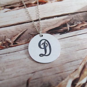 May include: A silver necklace with a round pendant featuring a cursive letter D.