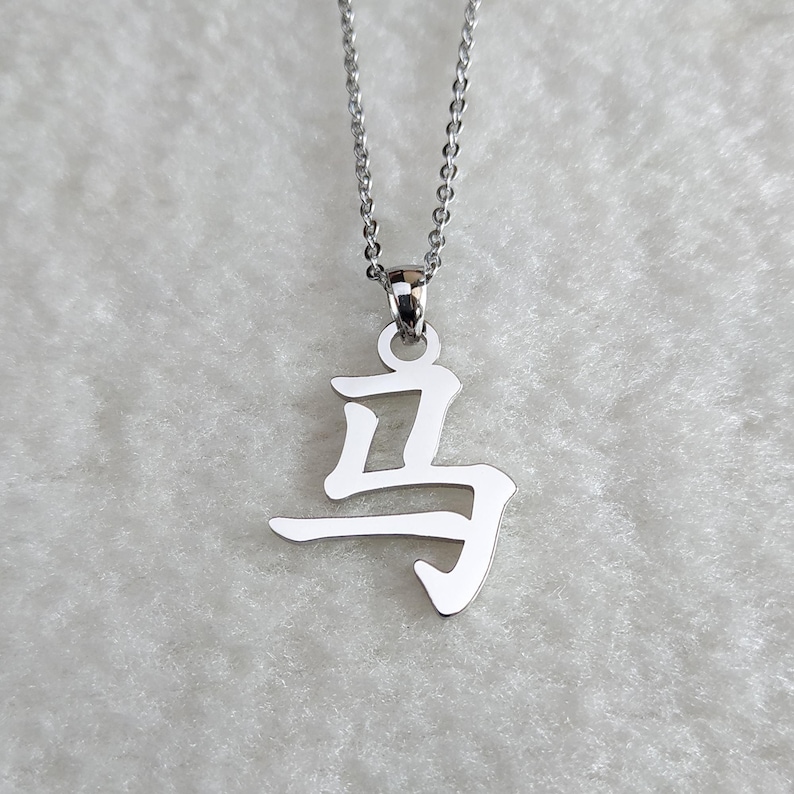 May include: A silver necklace with a pendant featuring the Chinese character for "horse".