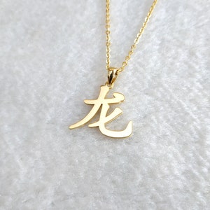 May include: Gold necklace with a pendant featuring the Chinese character for "long" in a stylized calligraphy font.
