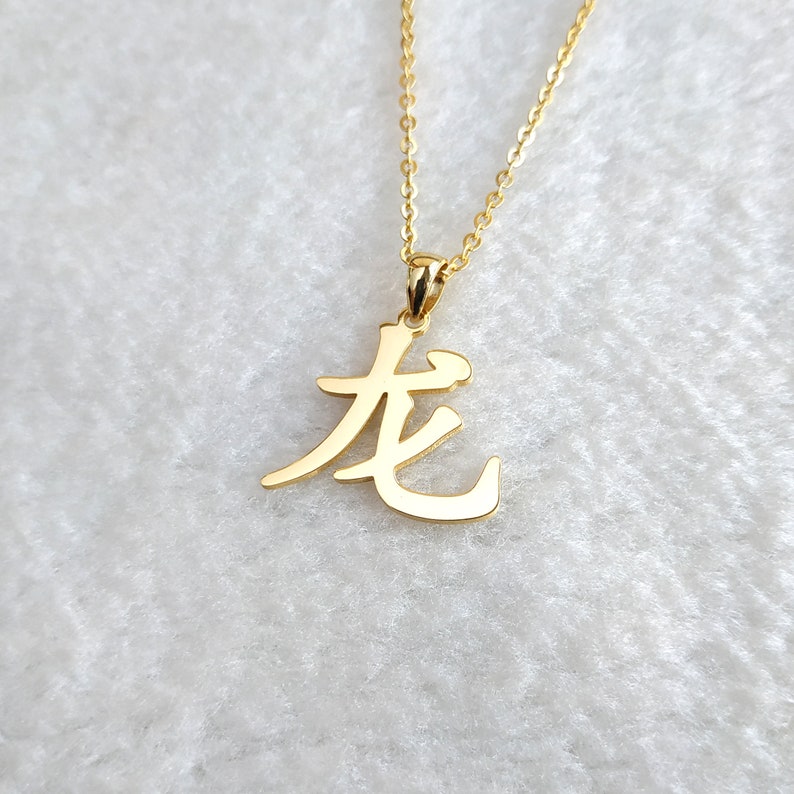 May include: Gold necklace with a pendant featuring the Chinese character for "long" in a stylized calligraphy font.