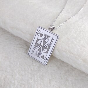 May include: Silver pendant necklace. The pendant is rectangular and features the Jack of Hearts playing card design. The card's details are engraved, including suit symbols and the letter "J". The necklace chain is also silver, creating a cohesive look.