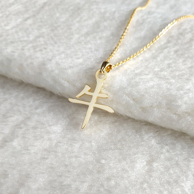 May include: Gold necklace with a pendant featuring the Chinese character for "ox".