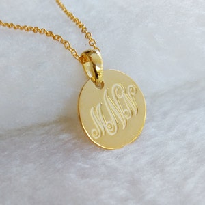 May include: A gold necklace with a round pendant featuring a monogram of the letters "M N" in a cursive script.