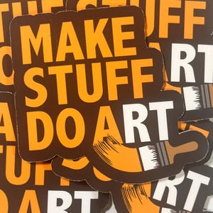 May include: A collection of stickers with the words "MAKE STUFF DO ART" in orange block letters on a dark brown background. A paintbrush graphic is included. The stickers are square with rounded corners.