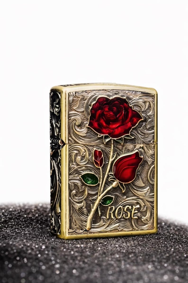 Op de afbeelding: Een vintage aansteker met een gedetailleerd bloemmotief. De aansteker heeft een rode roos met groene bladeren en het woord "ROSE" op de voorkant. Het metaal heeft een goud- en zilverafwerking.