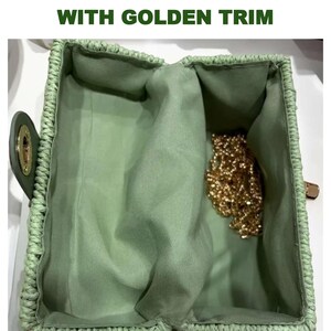 K&ouml;nnte beinhalten: Eine Vintage-Strohhandtasche mit goldenen Verzierungen. Die offene Handtasche ist hellgr&uuml;n mit passendem Innenfutter. Im Inneren ist eine goldene Kette zu sehen. Der Text "VINTAGE STRAW HANDBAG WITH GOLDEN TRIM" befindet sich oben im Bild.