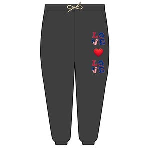 May include: Dark gray sweatpants with a drawstring waist. The word "LOVE" is vertically printed on the left leg in red, white, and blue, with a red heart in the center. The letters are decorated with stars and stripes.
