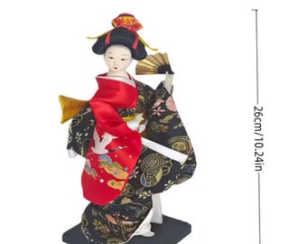 Op de afbeelding: Een 30 cm Japanse Geisha pop met een waaier en rode en zwarte kimono. De pop staat op een zwarte basis en is 26 cm hoog. De tekst "SHOP NOW!" wordt onderaan weergegeven.