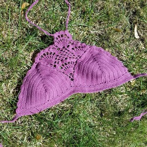 Pu&ograve; includere: Top halter in crochet viola con un delicato motivo a pizzo. Il top &egrave; steso su un letto di erba verde.