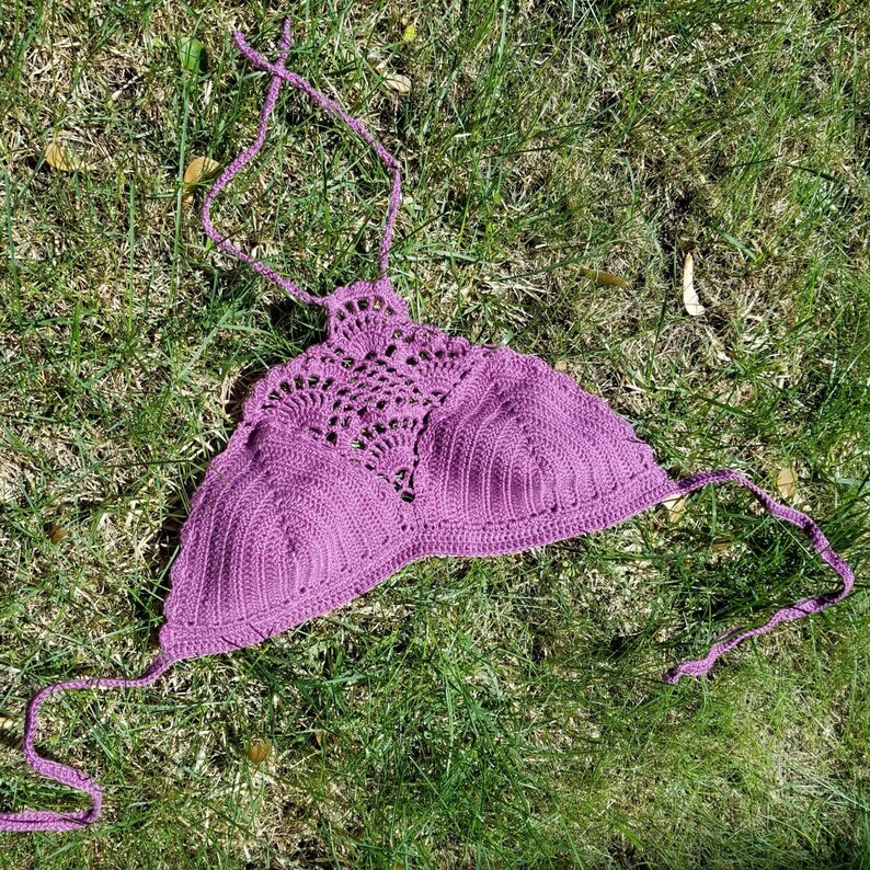 Pu&ograve; includere: Top halter in crochet viola con un delicato motivo a pizzo. Il top &egrave; steso su un letto di erba verde.