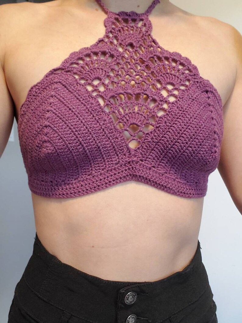 Pu&ograve; includere: Un top halter in crochet viola con un design delicato e intricato. Il top &egrave; senza maniche e ha un'alta scollatura.