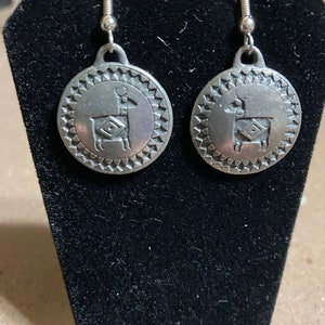 May include: A pair of silver earrings with a geometric design featuring a llama silhouette.