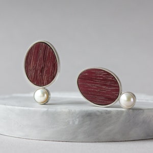 Not big earrings in the shape of an oval and a circle under it. The burgundy-colored oval is a wood inlay. The circle is a pearl.