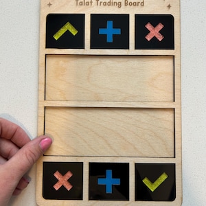 Può includere: Una tavola da gioco rettangolare in legno denominata Talat Trading Board, dotata di due ampi spazi orizzontali vuoti e sei quadratini neri con simboli intarsiati. I simboli includono segni più blu, spunte gialle glitterate e croci rosa glitterate.