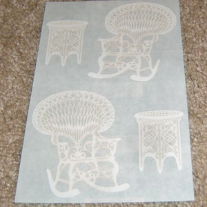 May include: Two white, decorative, wicker rocking chairs and two matching side tables. The chairs and tables are intricately woven and have a delicate, vintage look.