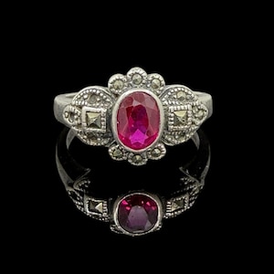 May include: A silver ring with a pink oval gemstone surrounded by marcasite stones.