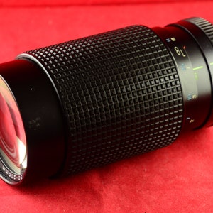 Op de afbeelding: Een zwarte camera lens met een zilveren ring en een getextureerde zwarte cilinder. De lens heeft een zoomring en een scherpstelring. De lens is gemarkeerd met de nummers 22, 16, 11, 8, 5.6, 4, 2.8 en 2.