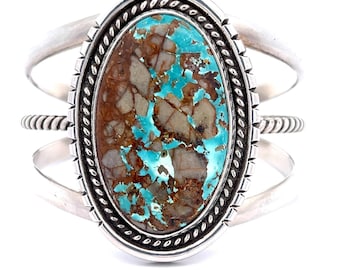 May include: A silver cuff bracelet with a large oval turquoise stone set in a silver bezel. The stone has a brown and blue marbled pattern. The bracelet has a twisted wire design on the sides.