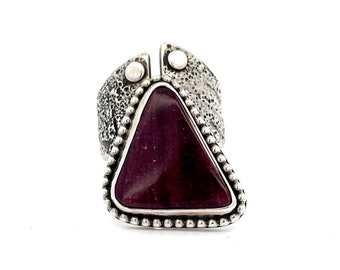 May include: A silver ring with a triangular purple stone set in a beaded bezel. The ring band is textured and has two small silver accents.