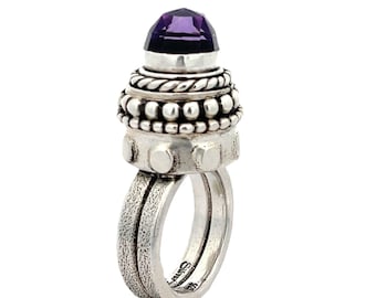 May include: A silver ring with a purple amethyst gemstone set in a dome-shaped top. The ring has a textured band and a beaded design around the gemstone.