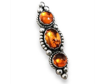 May include: A silver brooch with three amber stones set in a beaded design.