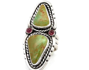 May include: A sterling silver ring featuring two triangular green turquoise stones with brown matrix, accented by two small round red gemstones. The metal setting displays a twisted rope border and a notched edge, creating a layered design.