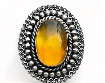 May include: An oval-shaped amber gemstone ring with a silver setting. The setting features a beaded border and a rope-like design.