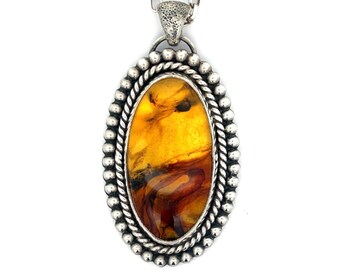May include: Silver pendant necklace with an oval amber stone. The amber has a mix of yellow and brown hues. The pendant is surrounded by a beaded border and a twisted rope design. The chain is silver.