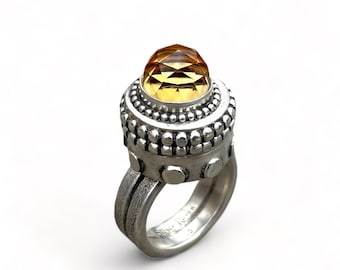 May include: A silver ring with a large, faceted, yellow gemstone set in a beaded bezel. The ring has a textured band and the words "Silver Acorn" are engraved on the inside of the band.