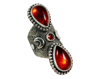 May include: A silver ring with three red gemstones. The ring has a textured surface and a design of crescent moons.