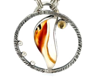May include: A silver necklace with a circular pendant featuring a brown and white agate stone, a small yellow gemstone, and three silver beads.